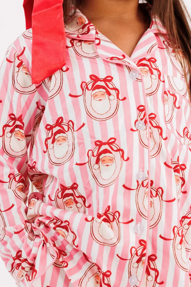 A close-up of a pink and white striped pajama shirt with a red and white Santa Claus face print, featuring a red tie-neck detail.