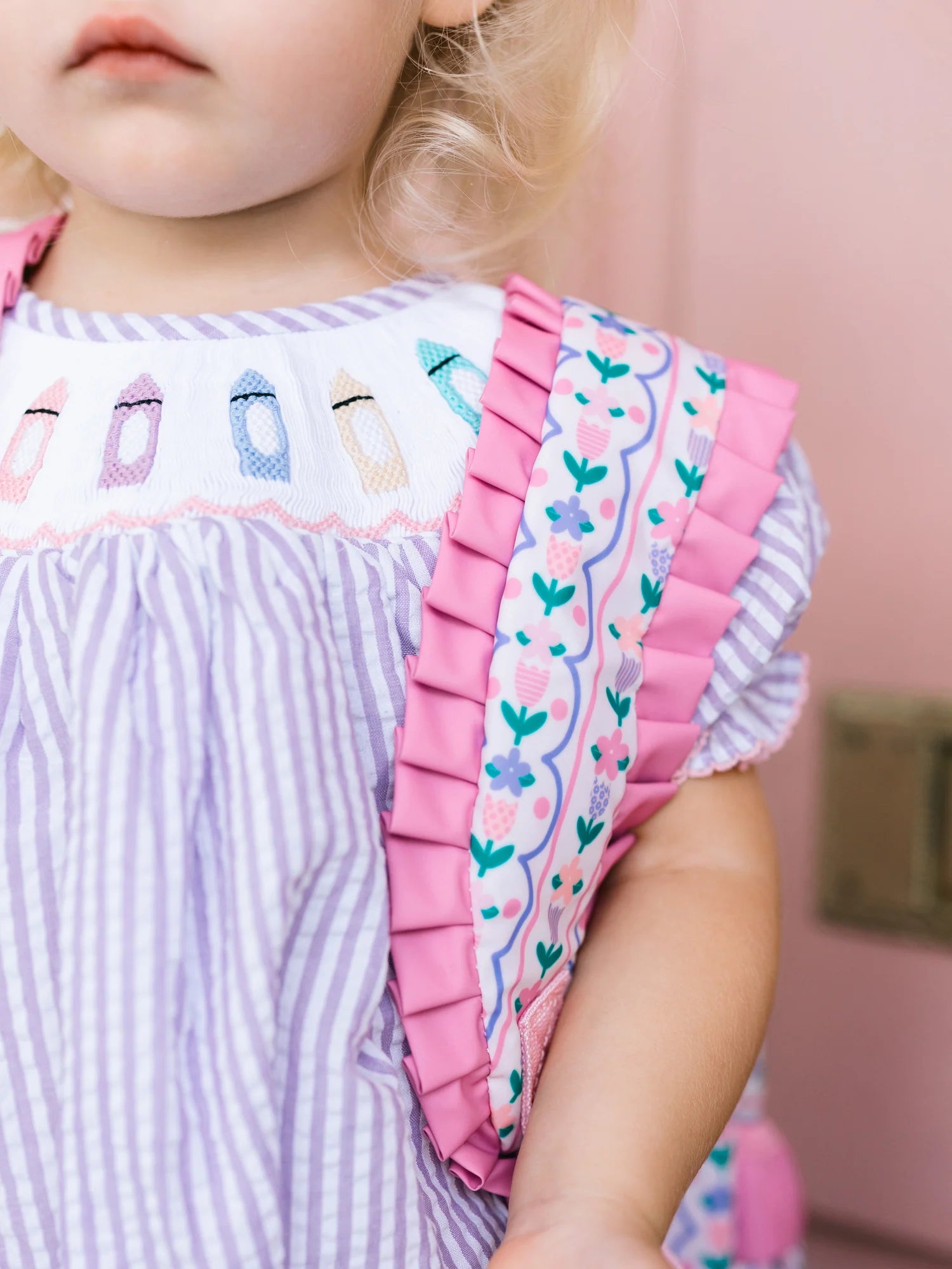 Child wearing a dress with ruffled pink trim and embroidered details.