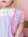 Child wearing a dress with ruffled pink trim and embroidered details.