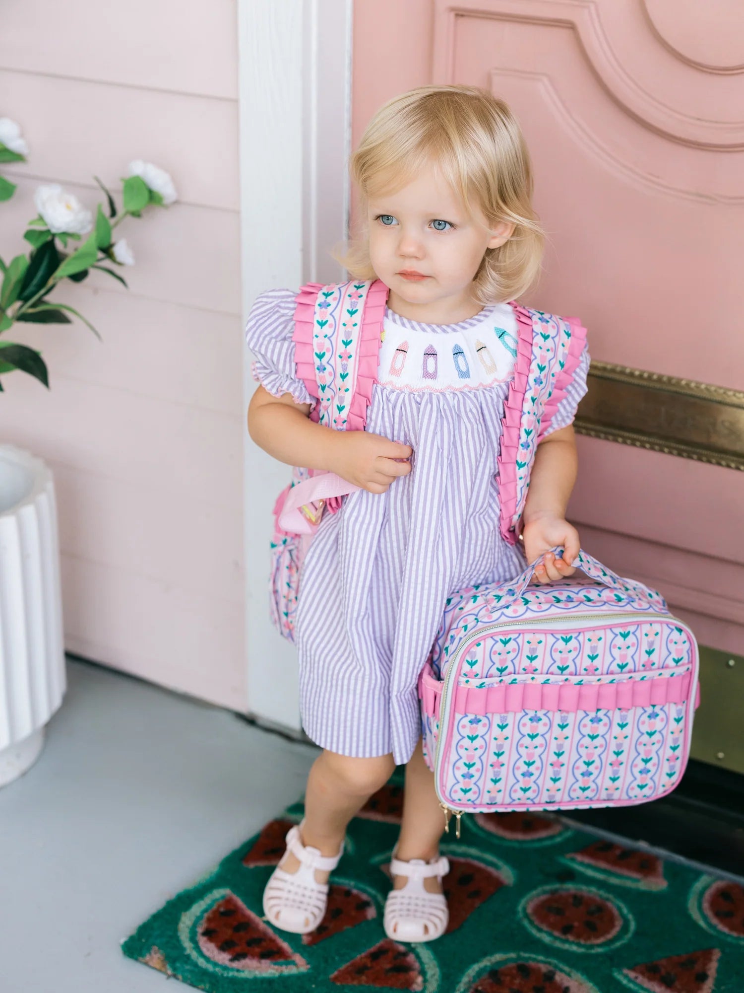 Child holding a pink and white lunchbox with decorative elements in a home setting.