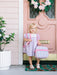 Young girl holding a colorful lunchbox in front of a pink door with floral decorations