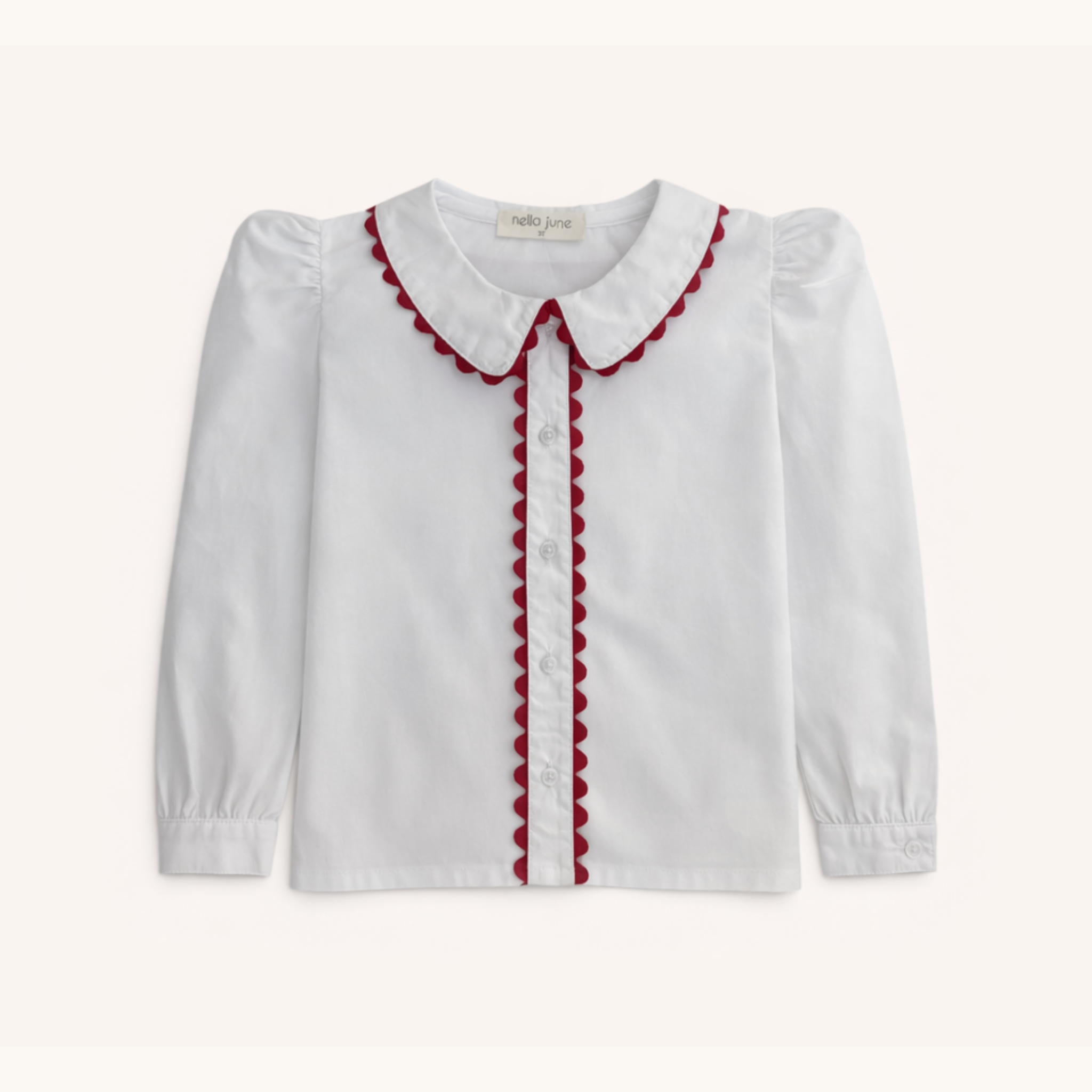 A white long-sleeve blouse for toddlers, featuring a Peter Pan collar and front placket trimmed with red scalloped fabric, shown against a light cream background.