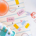 Stationery items including a pink eraser, glue stick, and scissors on a striped background.