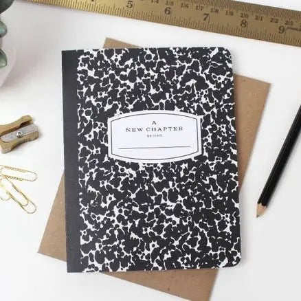 Notebook with black and white pattern and 'A New Chapter' text on a white background with stationery items.