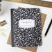 Notebook with black and white pattern and 'A New Chapter' text on a white background with stationery items.