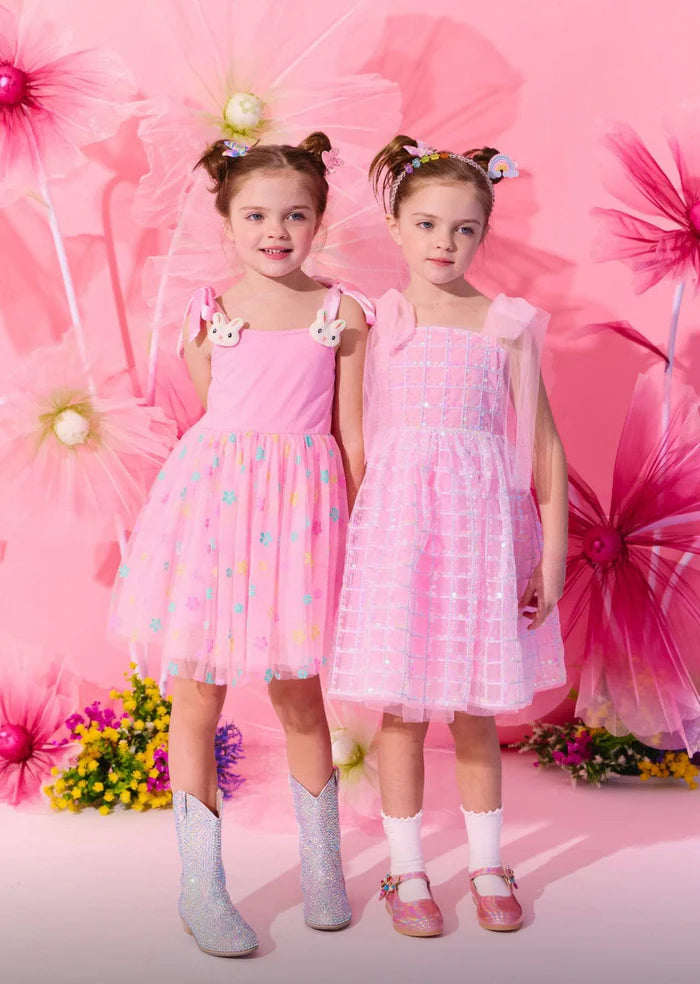 Two young girls in pink dresses standing against a pink floral background