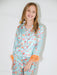 A young girl smiling while wearing a light blue satin pajama set with a colorful heart and star pattern, orange feather trim at the cuffs, and orange feather accents at the waist.