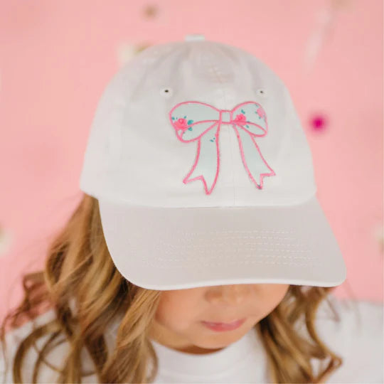 White cap with pink bow design on a pink background