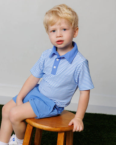 Child wearing a blue and white striped polo shirt and shorts sitting on a wooden stool.