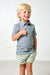 A young blonde boy smiling and giving a thumbs-up, wearing a blue and green striped short-sleeve polo shirt and light sage green shorts, standing against a plain white studio background.