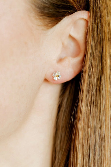 Close-up of an ear wearing a small floral earring with a blurred background