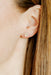 Close-up of an ear wearing a small floral earring with a blurred background
