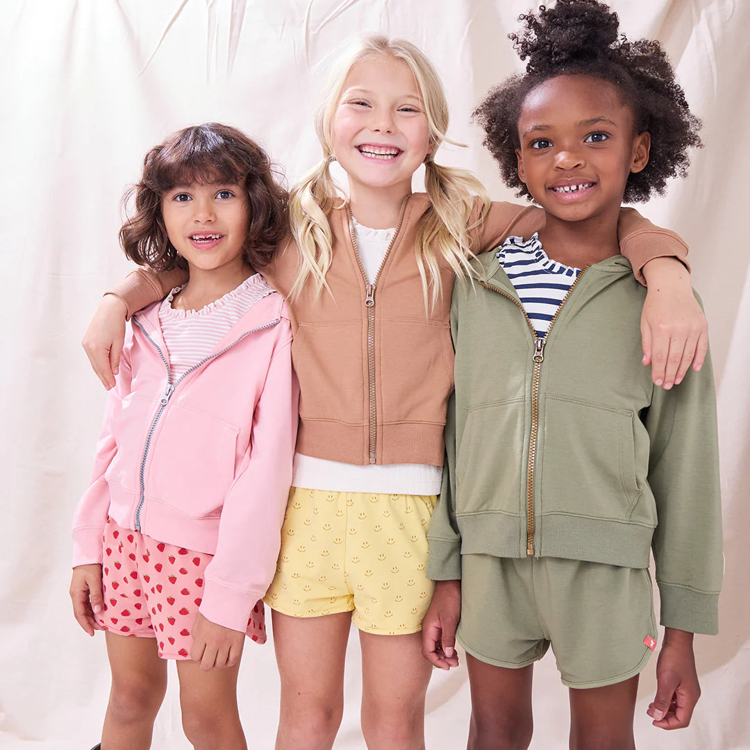 Three children wearing matching jackets and shorts standing together against a plain background