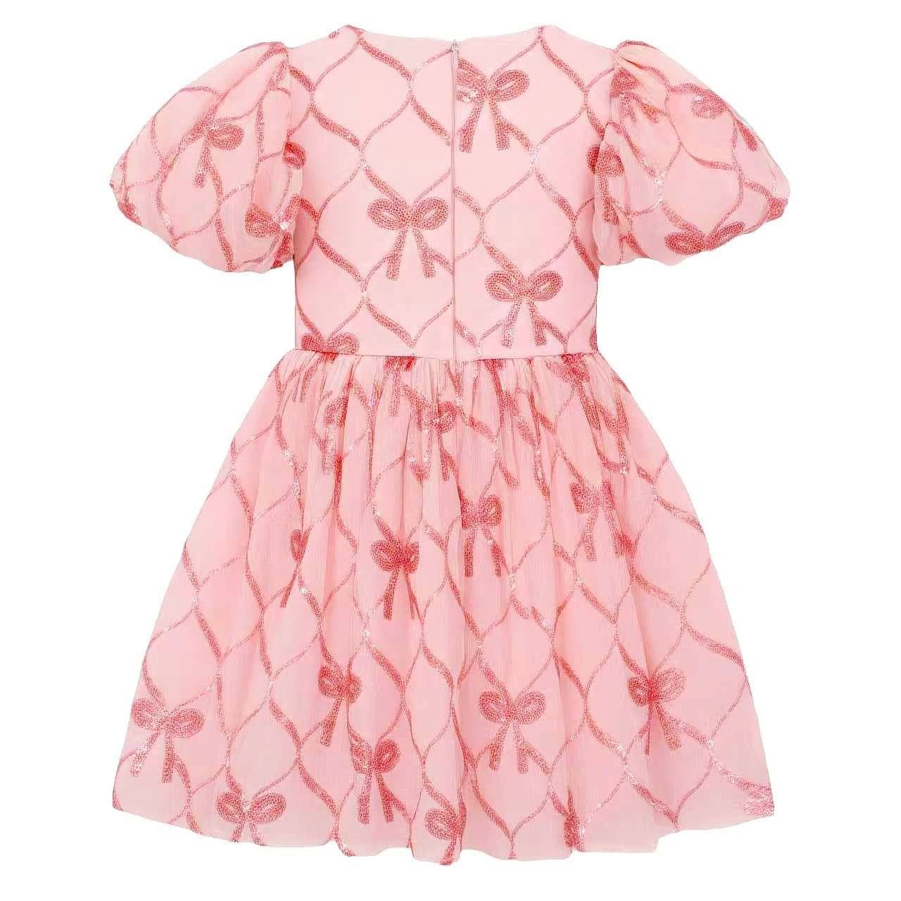 A pink short-sleeve dress with puff sleeves and a gathered tulle skirt, featuring an allover repeating pattern of shiny metallic bow motifs over a subtle diamond lattice background.