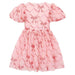 A pink short-sleeve dress with puff sleeves and a gathered tulle skirt, featuring an allover repeating pattern of shiny metallic bow motifs over a subtle diamond lattice background.