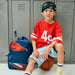Boy sitting next to a Sports Rodgers Backpack with a partial basketball and football on the front.