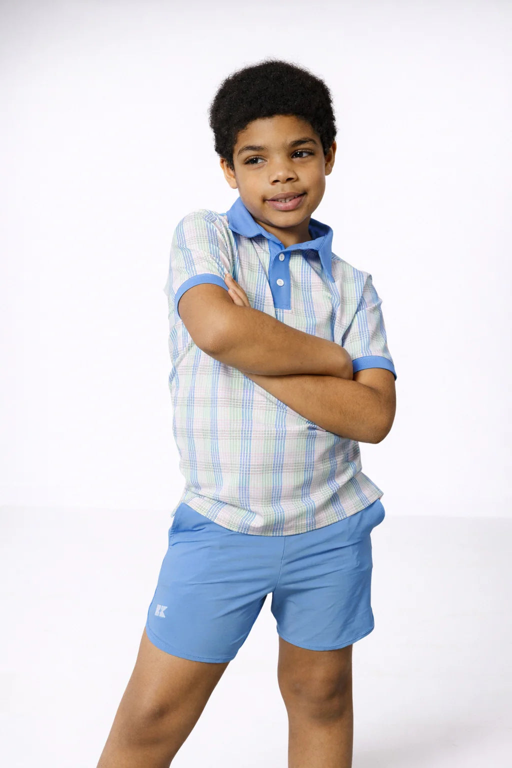 Child wearing a checkered shirt and blue shorts on a white background