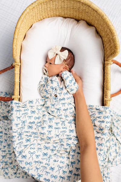 Baby in a Moses basket with a white bow, wearing a blue and white outfit.