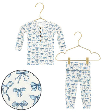 Children's long-sleeve shirt and pants with blue bow pattern on hangers against a white background.
