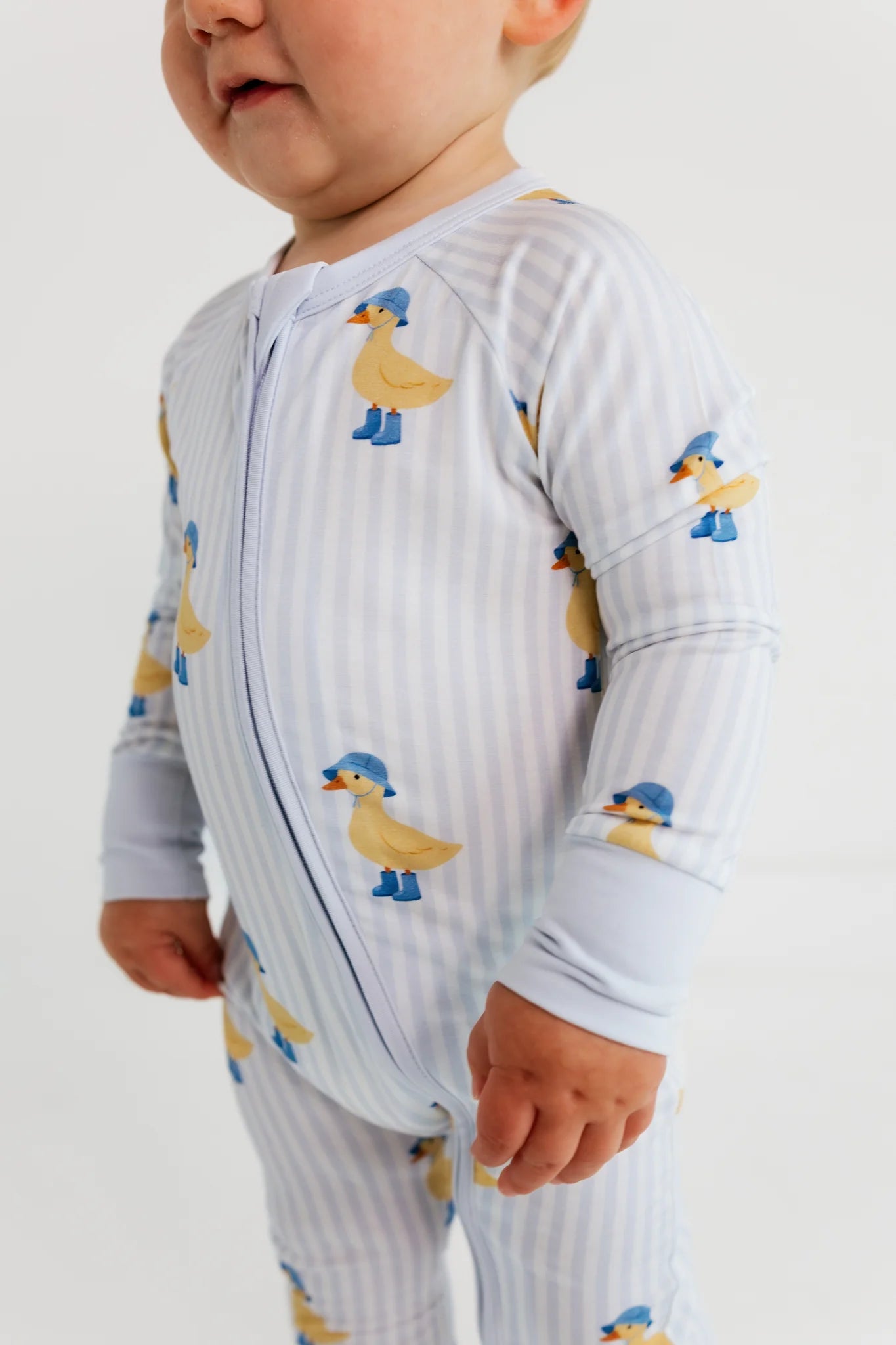 Baby wearing a onesie with duck pattern on a plain background