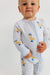 Baby wearing a light blue onesie with duck patterns on a plain background