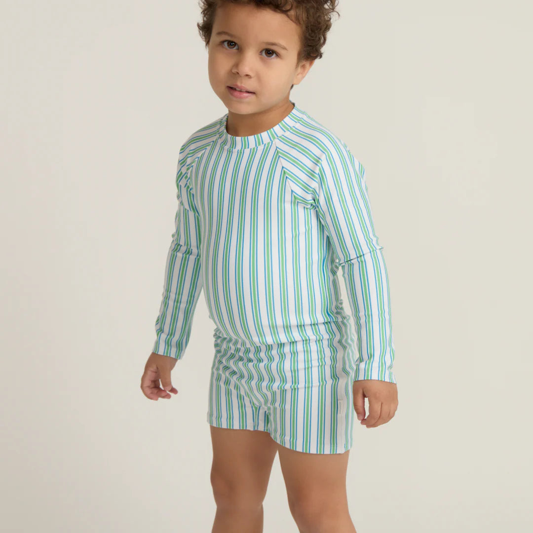 Child wearing a green and white striped shirt and shorts on a plain background