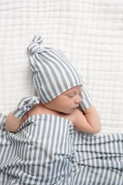 Newborn baby wrapped in a grey and white striped blanket and hat on a white textured background