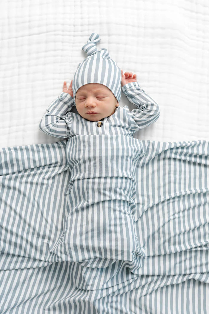 Newborn baby wrapped in a grey and white striped swaddle blanket with matching hat on a white background