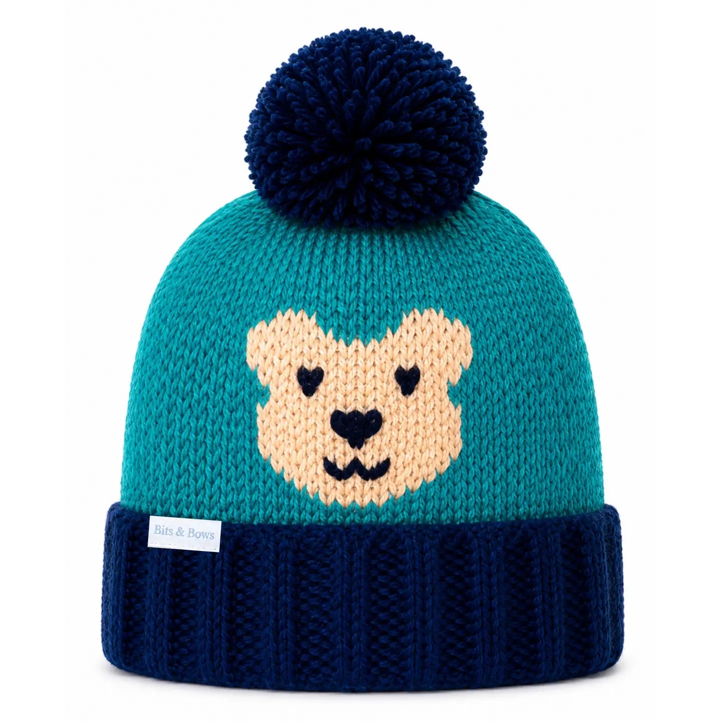 A teal and navy blue knit beanie hat with a dark navy pom-pom on top and a knitted bear face on the front. The bottom cuff is ribbed navy blue, and a small white tag is visible on the side.