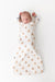 A sleeping newborn baby lying on their back, swaddled in a sleep sack printed with a repeating pattern of small tan teddy bears with blue accents, on a clean white background.