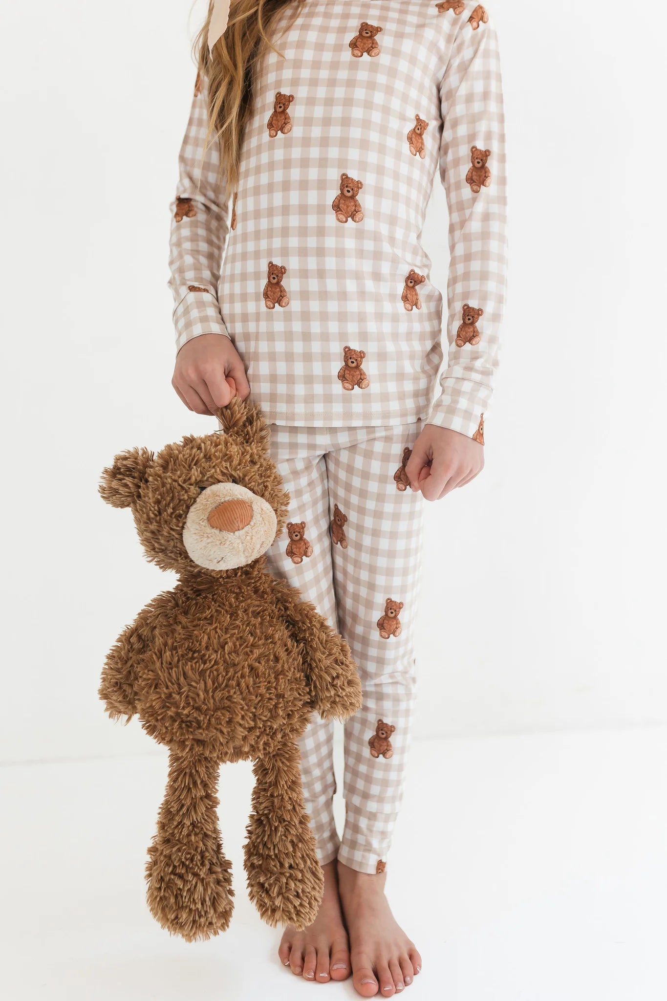 Person wearing a checkered pajama set with teddy bear patterns, holding a plush teddy bear.