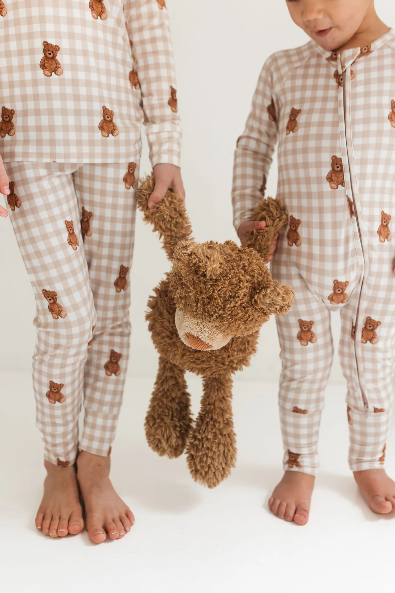 Two children wearing matching pajamas with teddy bear patterns, holding a plush teddy bear.
