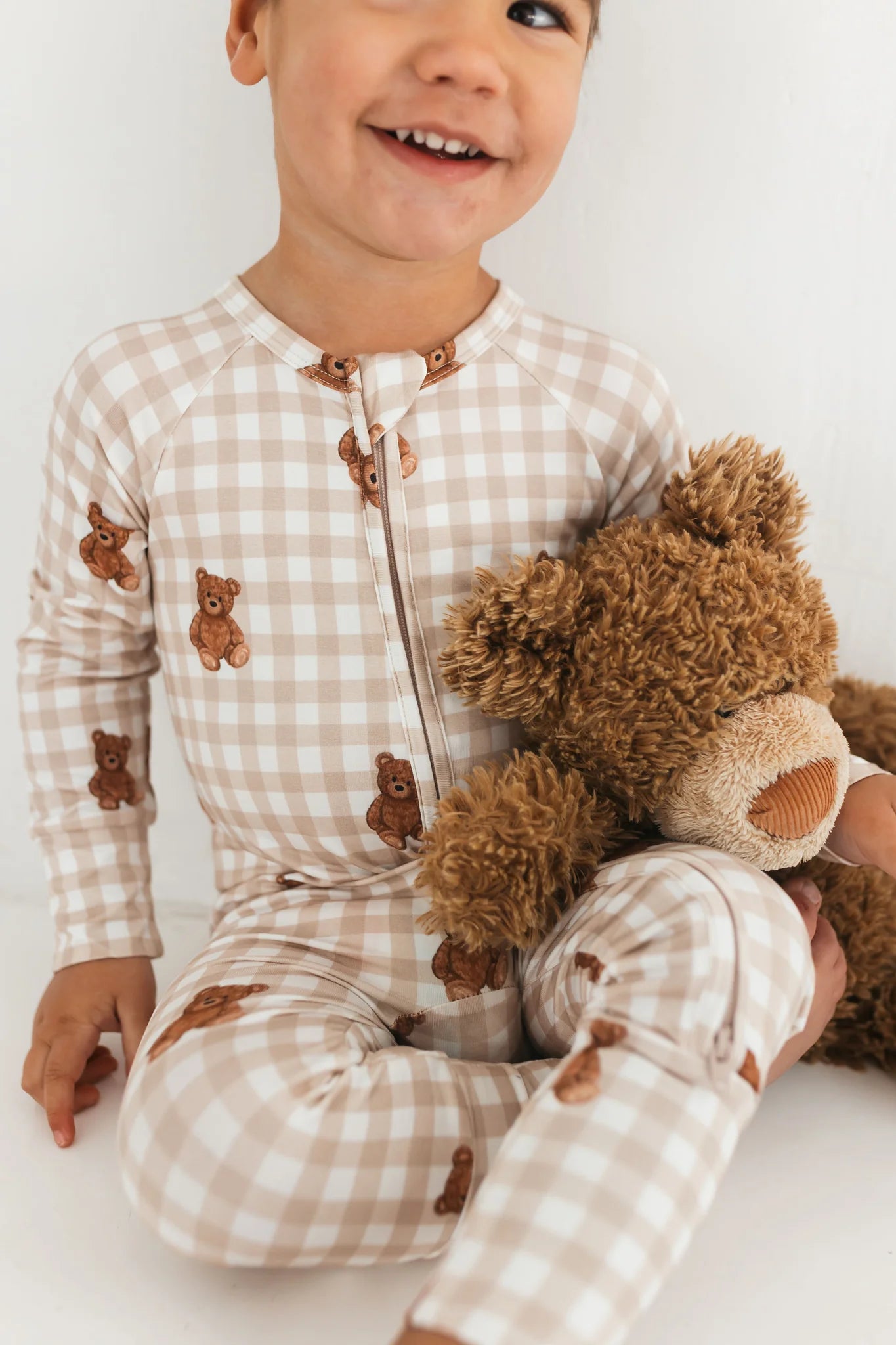 Child wearing a checkered outfit with teddy bear designs, holding a teddy bear.