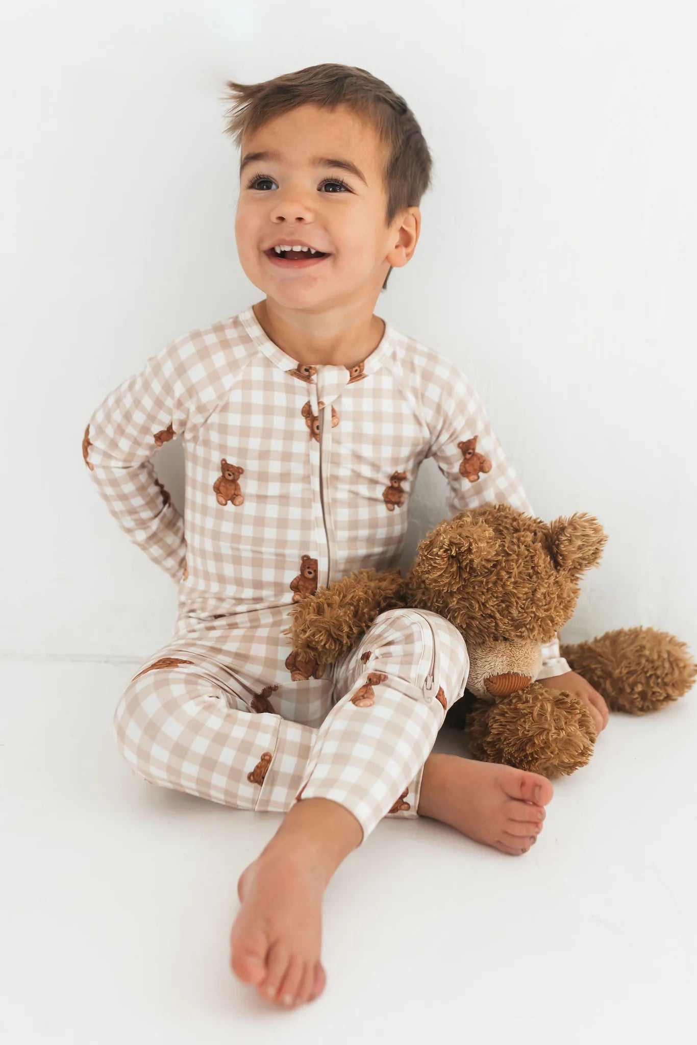 Child wearing a checkered outfit with teddy bear design, sitting on a white background