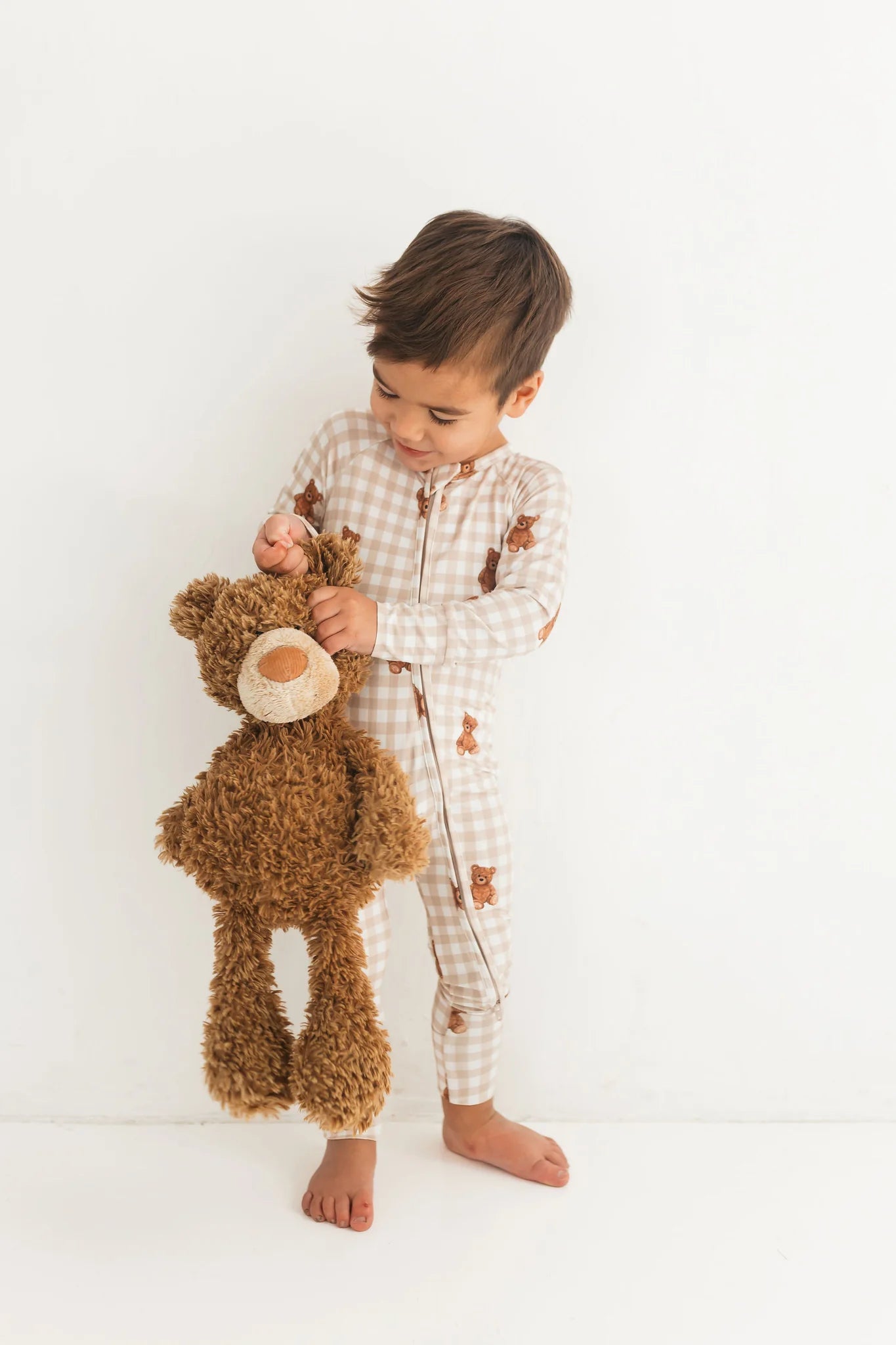 Child in checkered pajamas holding a teddy bear against a white background
