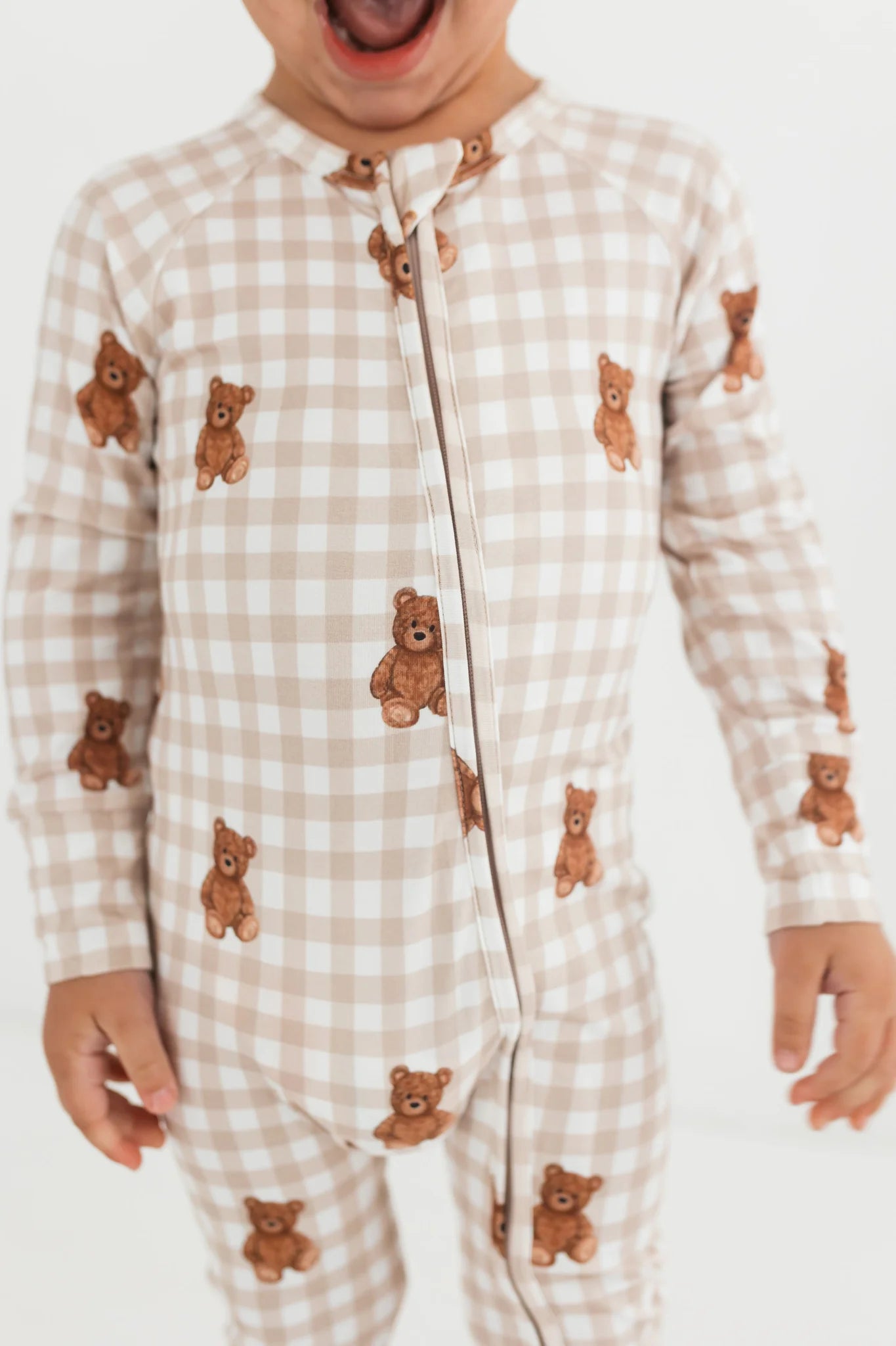 Child wearing a beige checkered onesie with teddy bear patterns on a white background