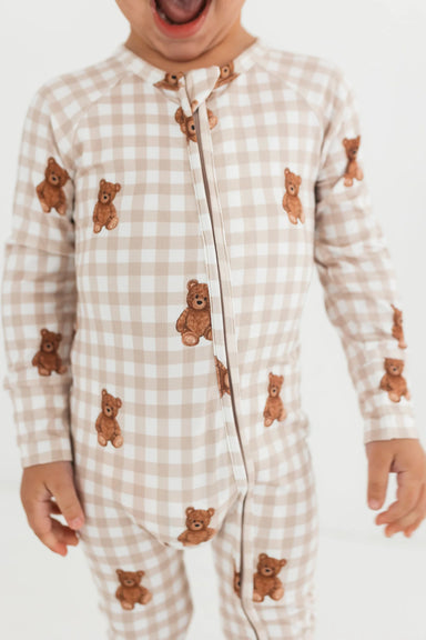 Child wearing a beige checkered onesie with teddy bear patterns on a white background