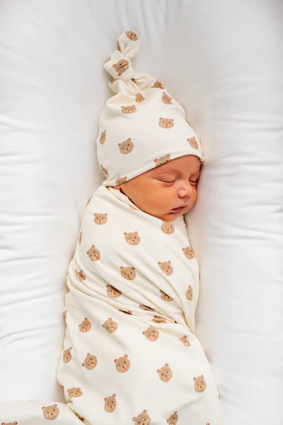 Newborn baby swaddled in a blanket with teddy bear pattern, wearing a matching headband.