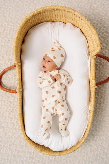 Newborn baby in a wicker crib with a white pillow and matching outfit.
