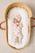Newborn baby in a wicker crib with a white pillow and matching outfit.