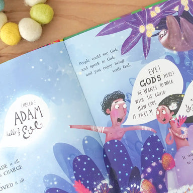 Open book with colorful illustrations of Adam and Eve, surrounded by decorative items on a wooden surface.