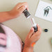 Two hands holding small bottles with black labels on a light surface.