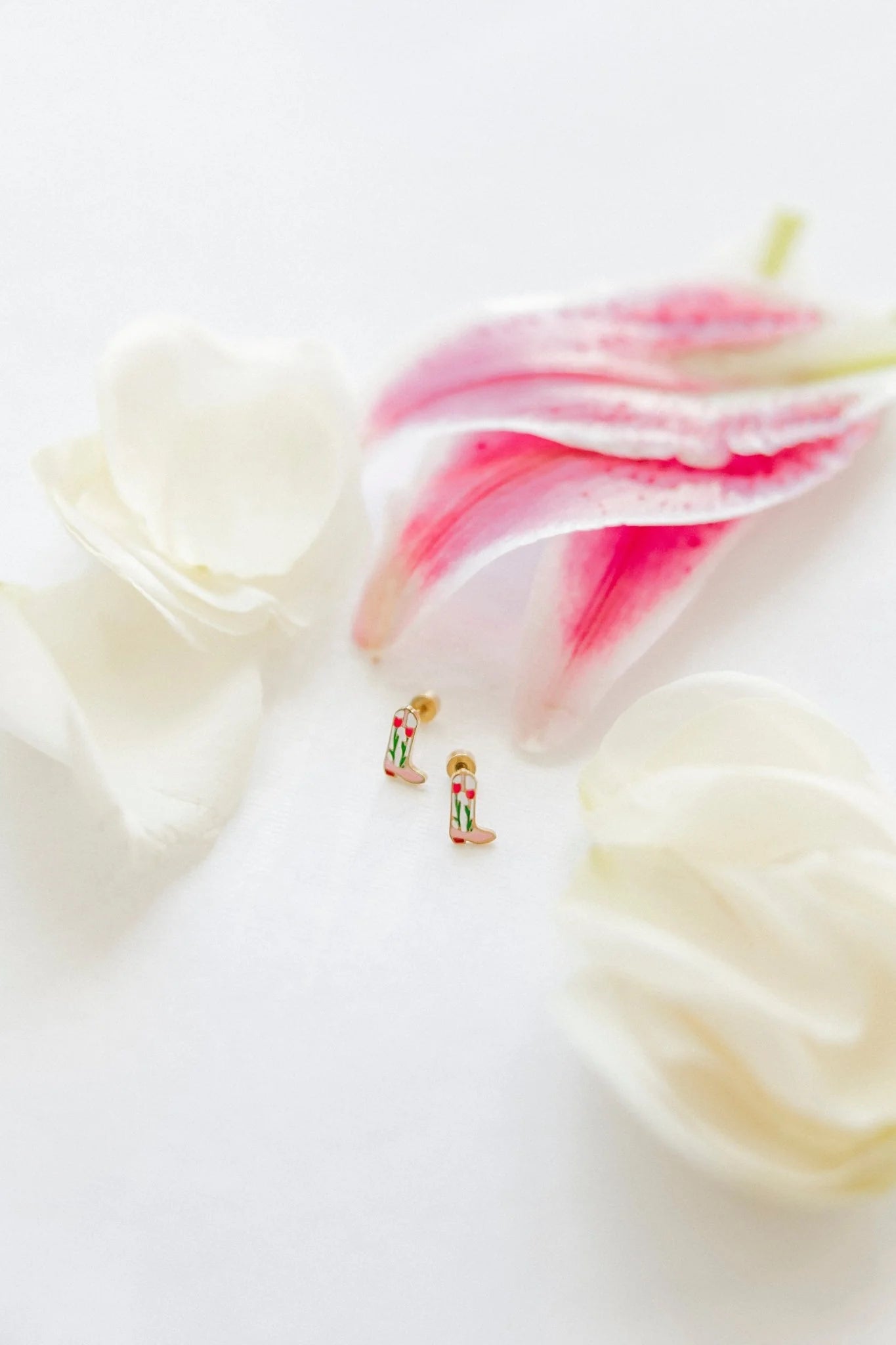 Small gold earrings on a white surface with pink flowers in the background