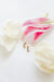 Small gold earrings on a white surface with pink flowers in the background