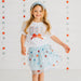 Young girl wearing a 'USA' t-shirt and light blue skirt with star patterns against a decorative background.