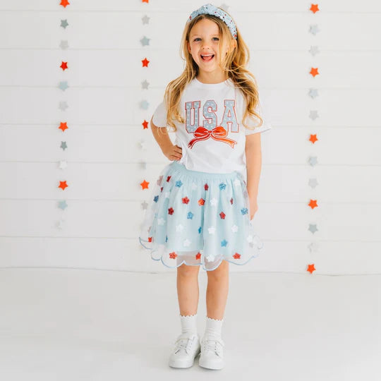 Young girl wearing a 'USA' t-shirt and floral skirt against a star-patterned background