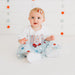 Baby sitting on a white blanket with a USA-themed outfit and headband against a star-patterned wall.