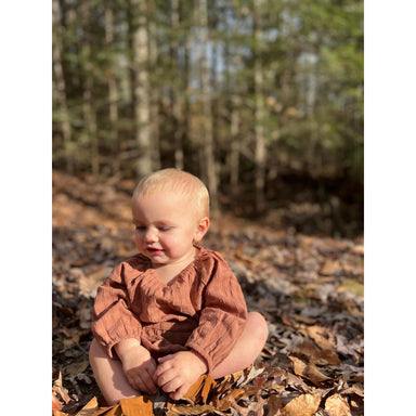 baby girl sitting up wearing rust colored long sleeve bubble romper