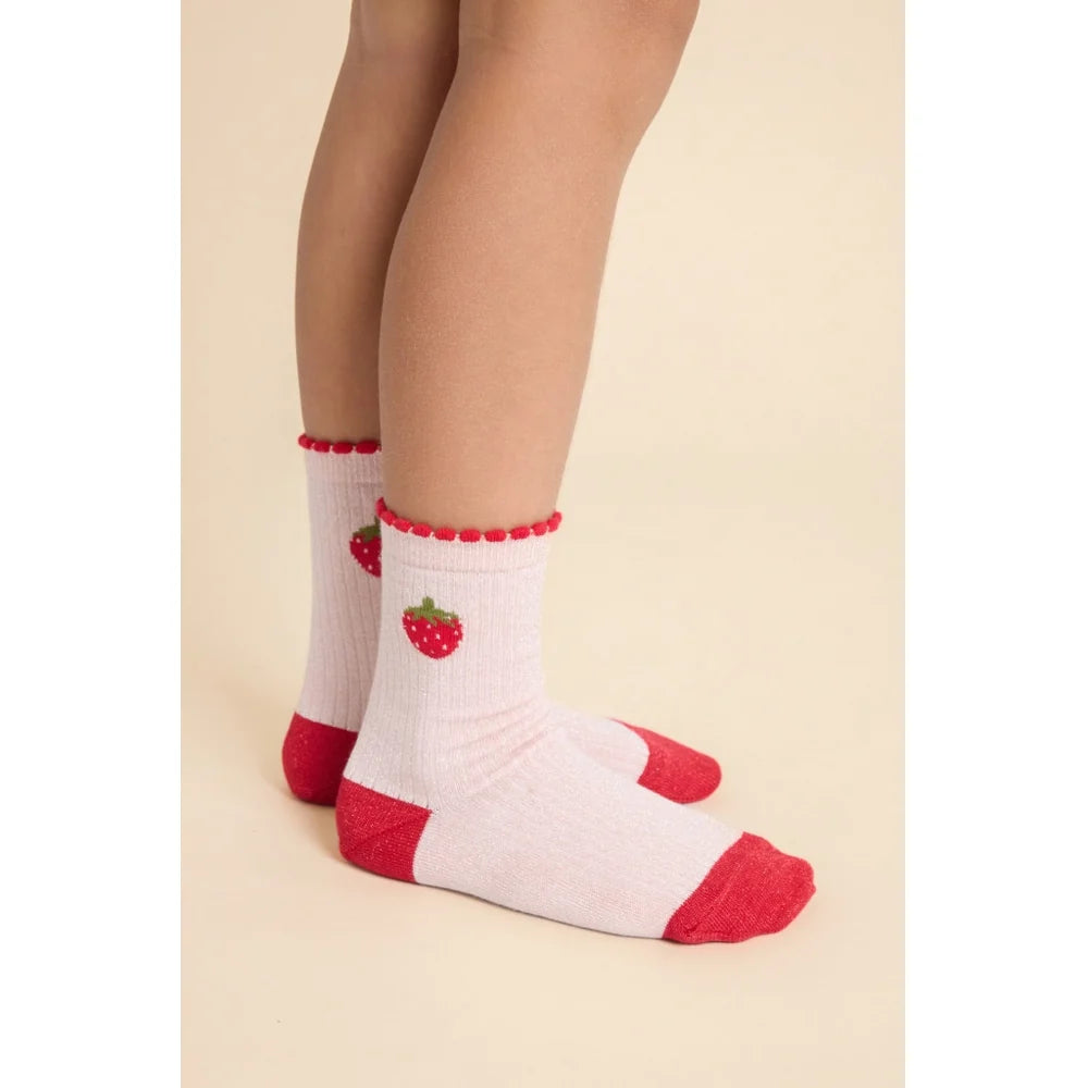 Pink crew socks with red toes, heels, and cuffs, featuring embroidered red strawberries, shown on a child's legs against a light beige background.
