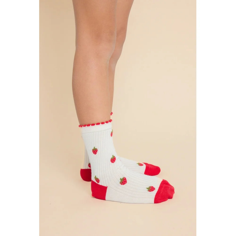 White ribbed crew socks with red toes, heels, and cuffs, decorated with small embroidered red strawberries, shown on a model's feet against a solid beige background.